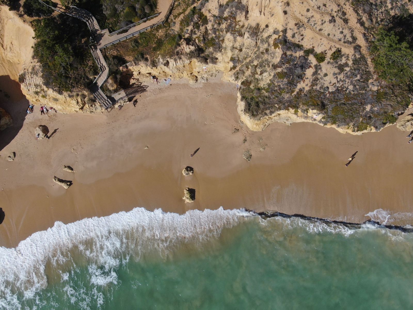 Aerial view of a sandy beach with rocky cliffs and rolling waves